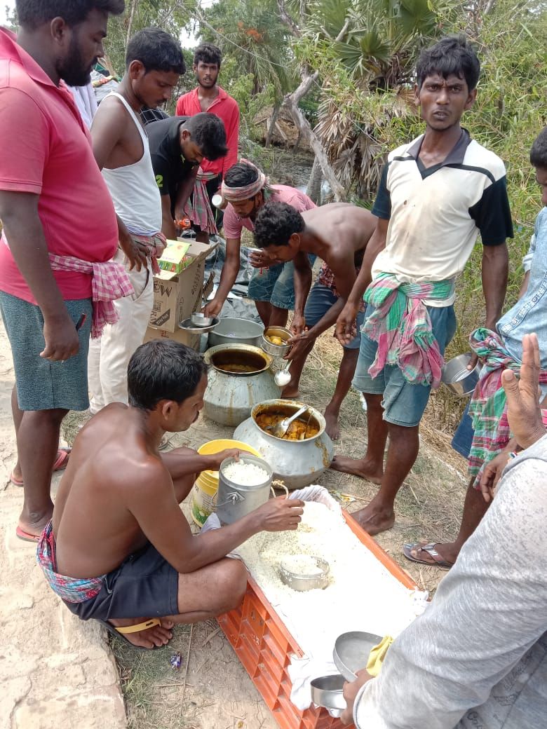 Volunteers serving hot khichuri from large pots on a river embankment