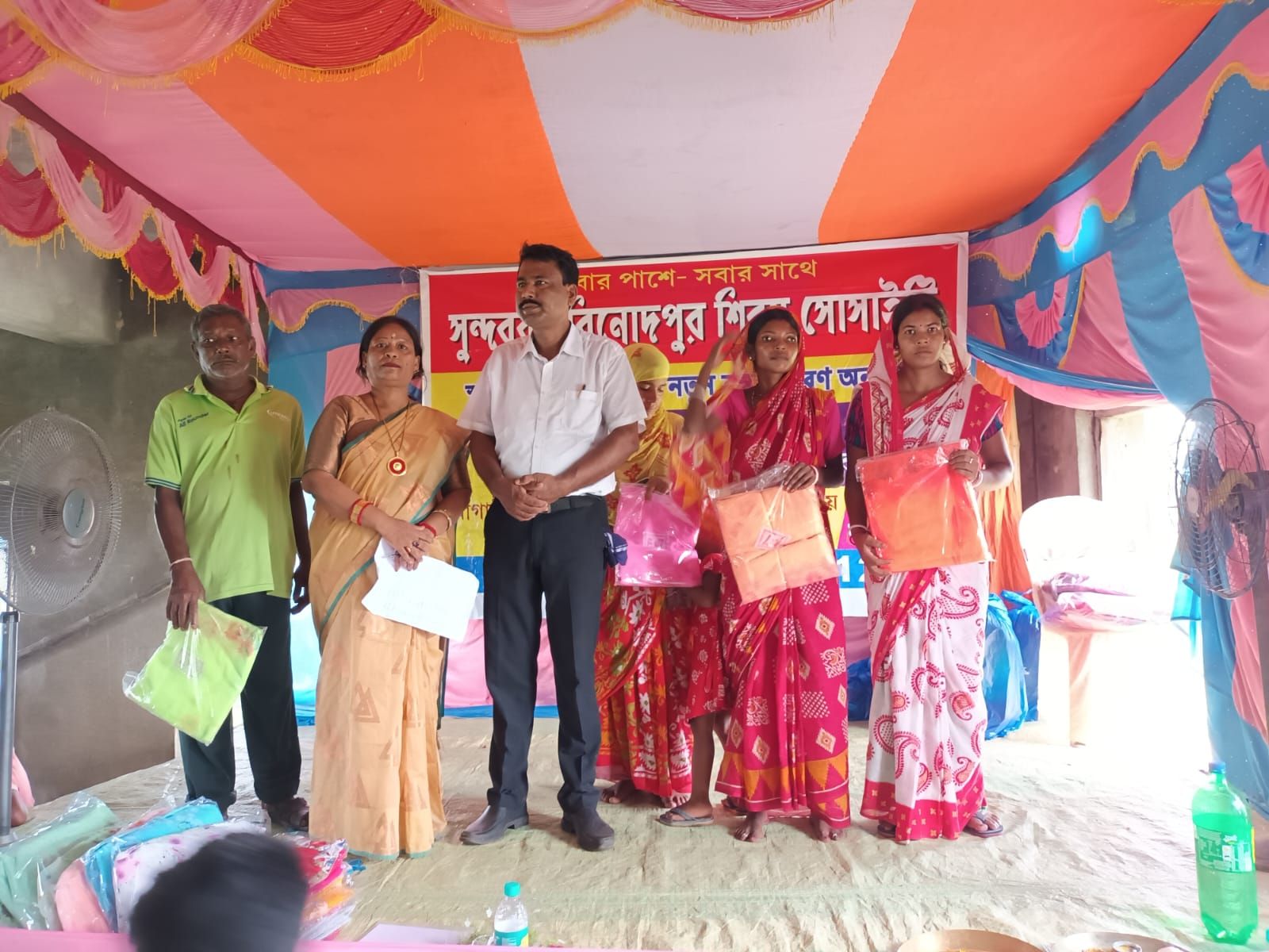 Women receiving new saris on stage under the society banner