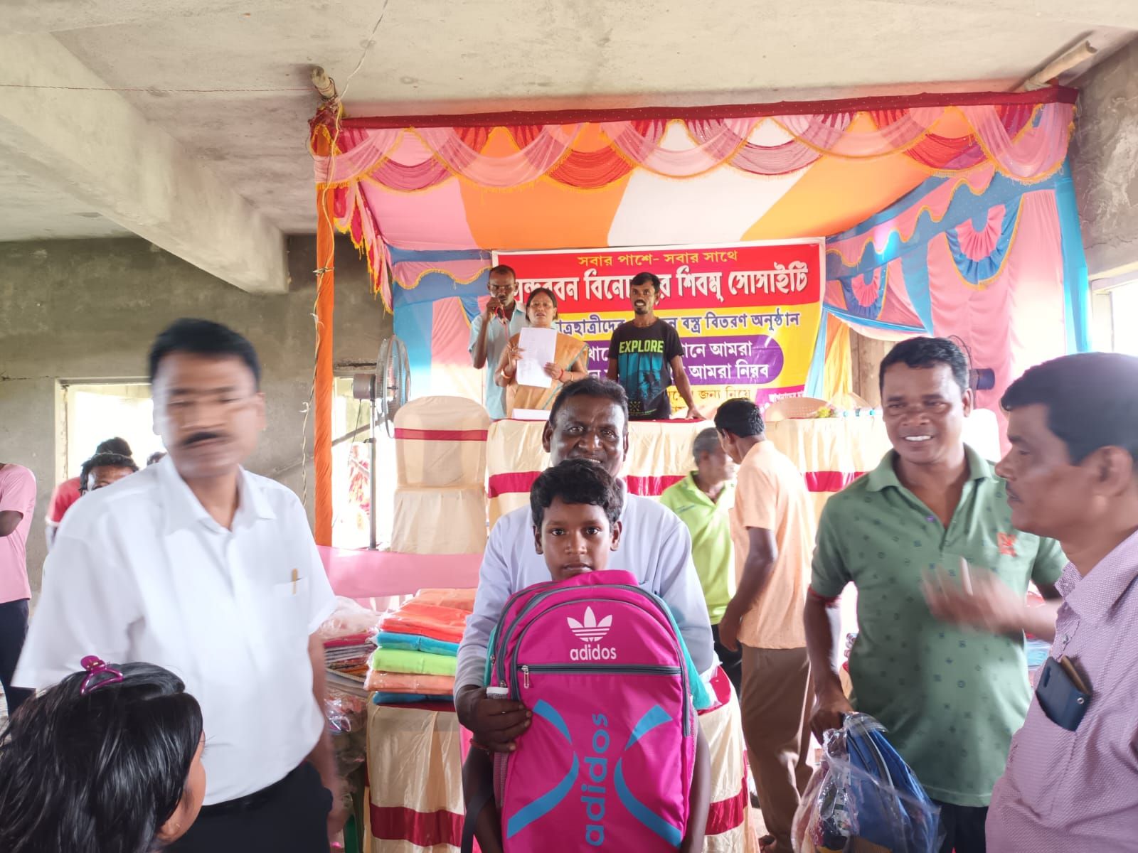 Society members handing a new school bag to a student at a community event