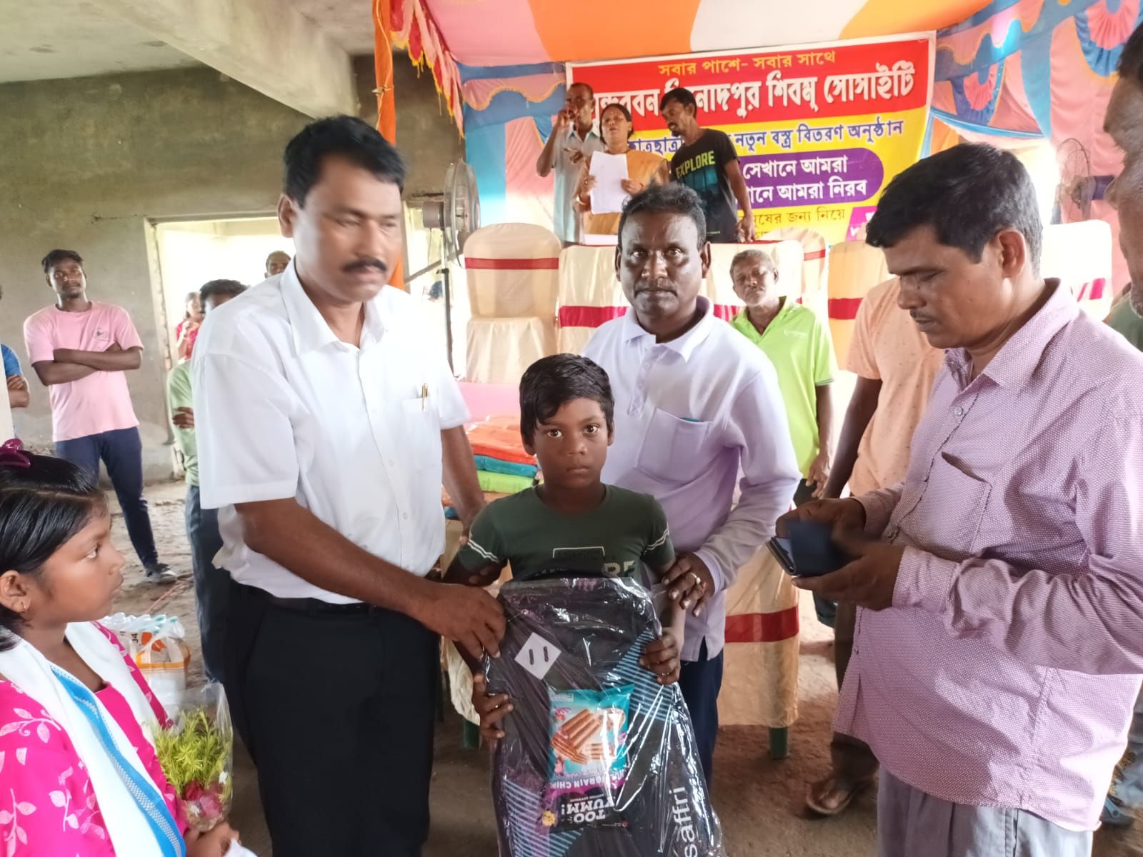 A boy receiving a school bag from society members on stage