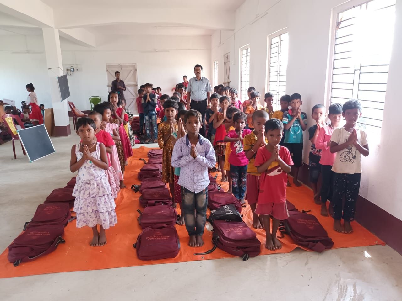 Children standing in rows beside new school bags laid out on the floor