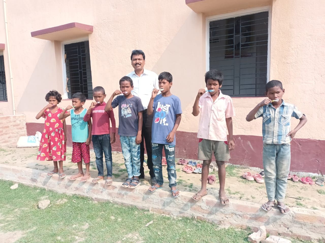 A volunteer teacher guiding children through a tooth-brushing drill outdoors