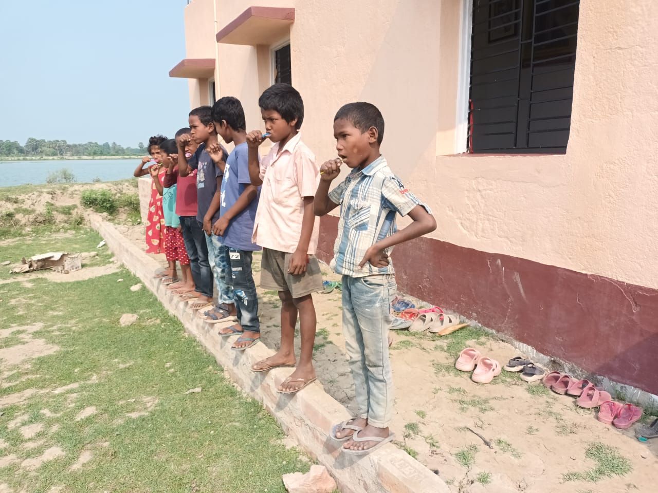 Children standing in a line outside a school building learning how to brush their teeth